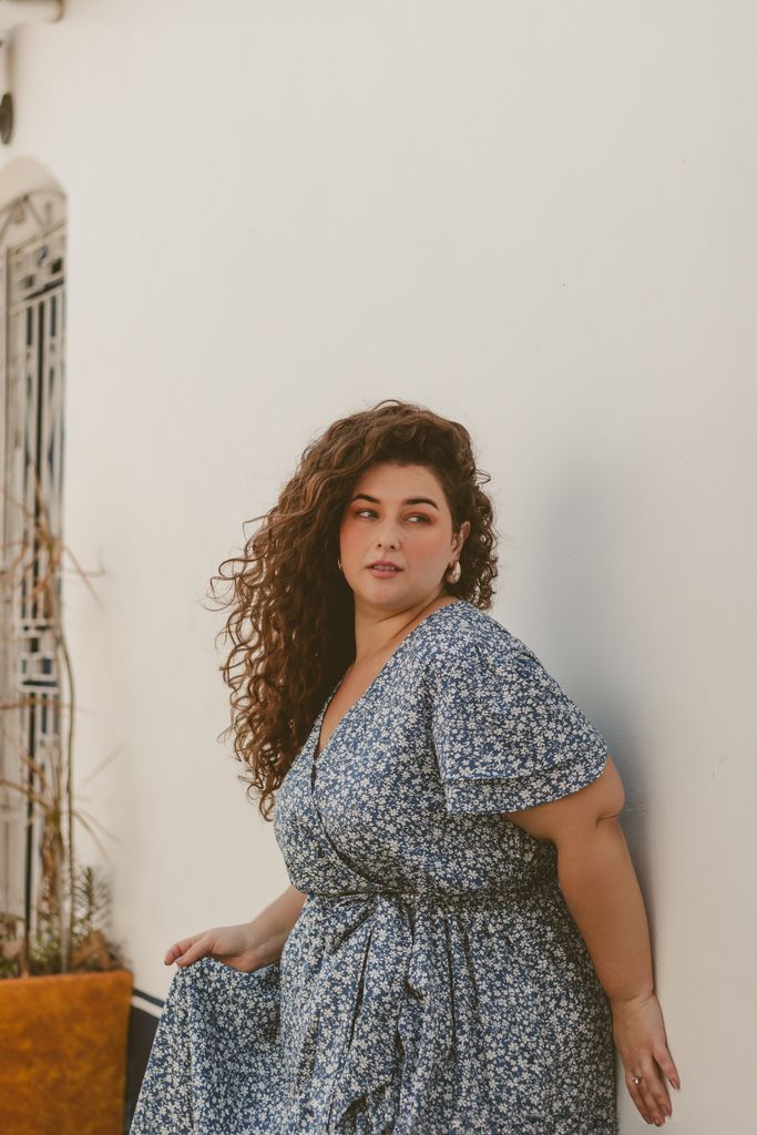 Confident woman with curly hair poses in a floral dress against a white wall in Rio de Janeiro.