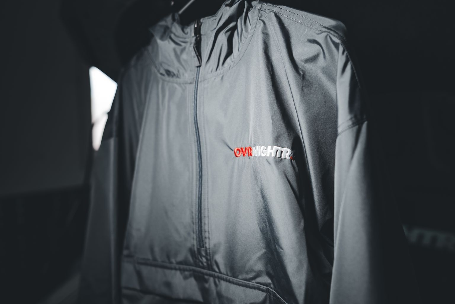 Gray windbreaker jacket with 'OVRNIGHTR' logo displayed in selective focus.