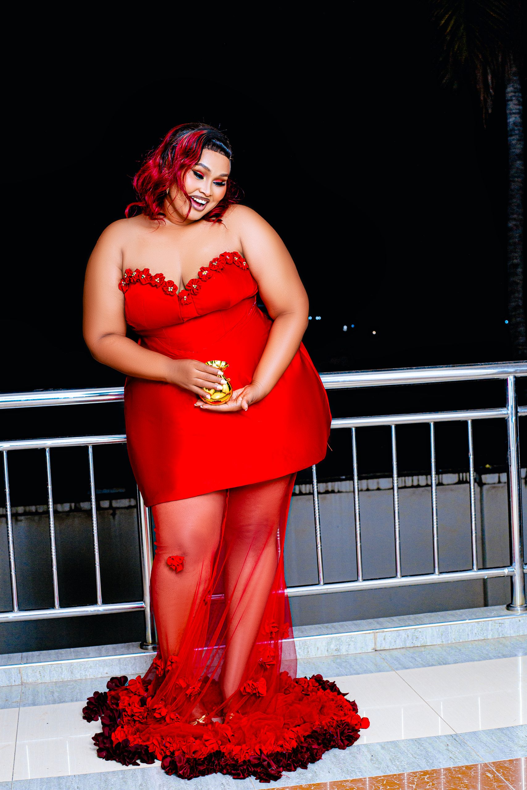 Stylish woman in a glamorous red evening dress posing outdoors at night.
