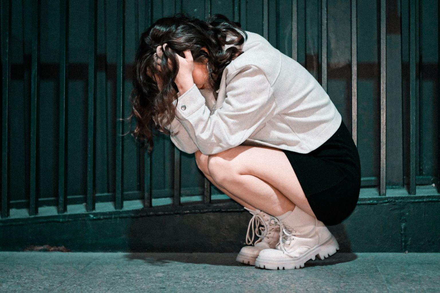 Woman crouching with head in hands against city wall, expressing deep contemplation.