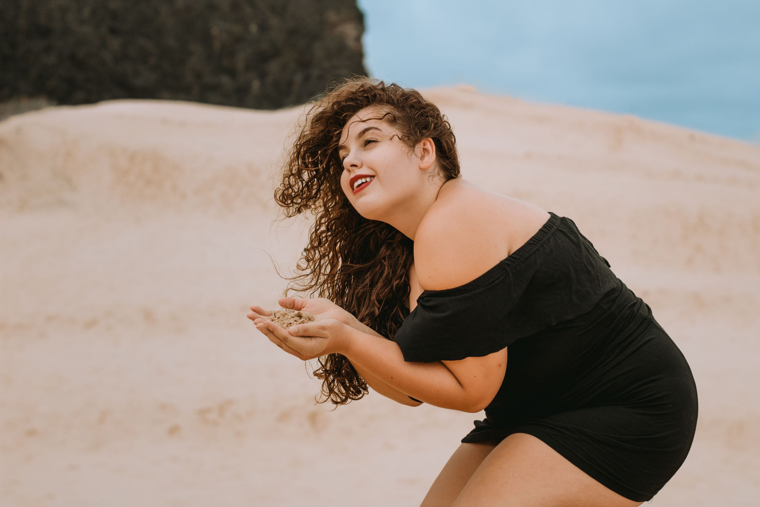 Woman in a black dress at the beach enjoying sand. Perfect for summer and leisure themes.