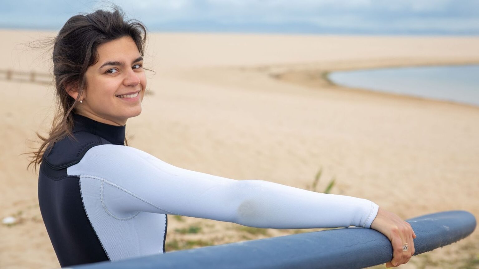 A young woman in a wetsuit prepares to surf on a sandy beach in Portugal exuding joy and adventure