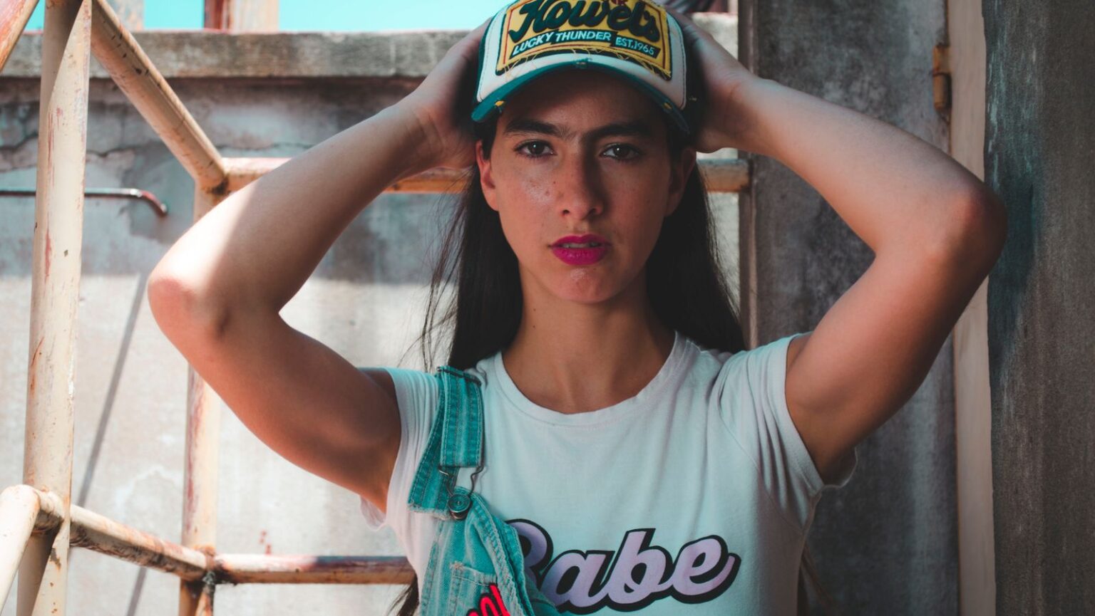 Woman wearing Trucker hat baby tee and denim overall