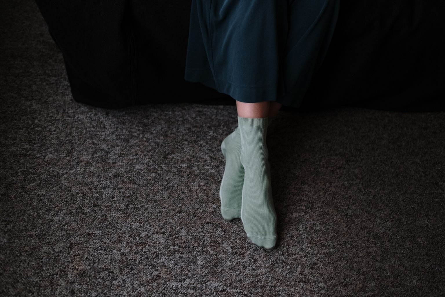 From above of crop anonymous female in socks sitting with crossed legs on carpet in house