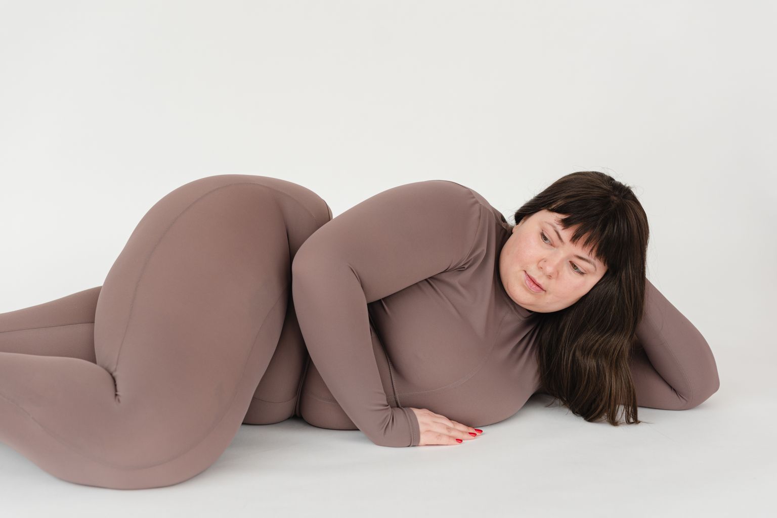 High angle of serious plus size female with long hair leaning on hand while lying against white background