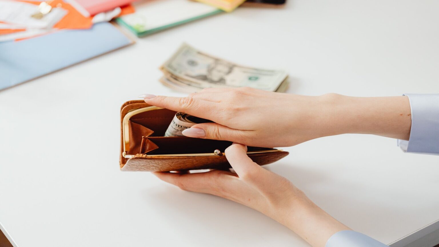person putting money in a brown wallet 7680475