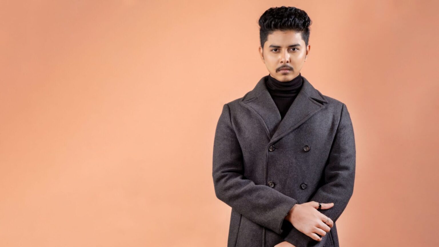 Sophisticated portrait of a man wearing a gray overcoat against a warm backdrop.