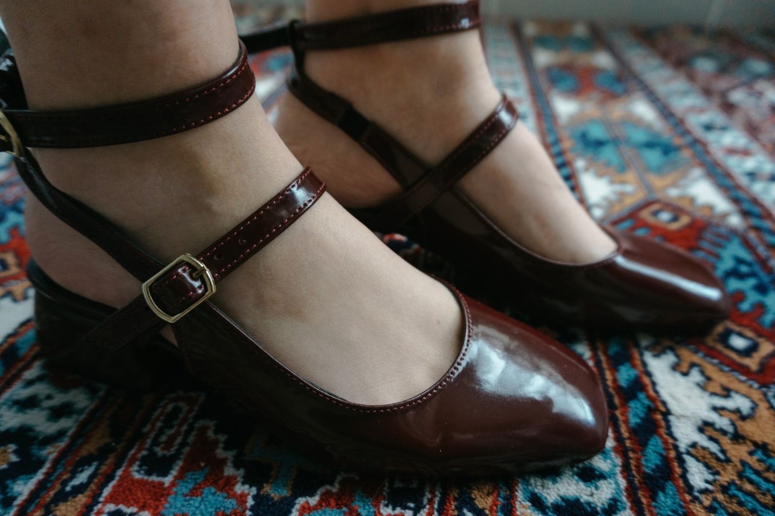 Stylish brown leather shoes with ankle straps on a colorful patterned rug.