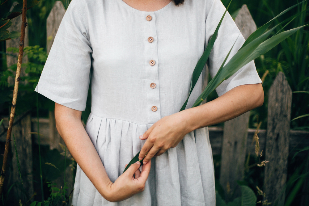 stylish girl in linen dress holding green leaf at wooden fence a 255240914 S