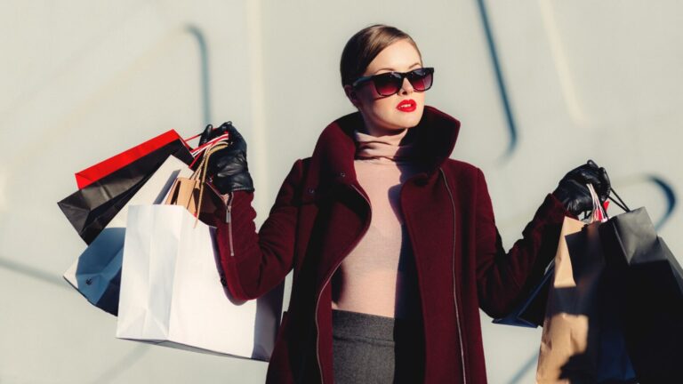 Stylish young woman in sunglasses carrying shopping bags outdoors. Elegant fashion statement.