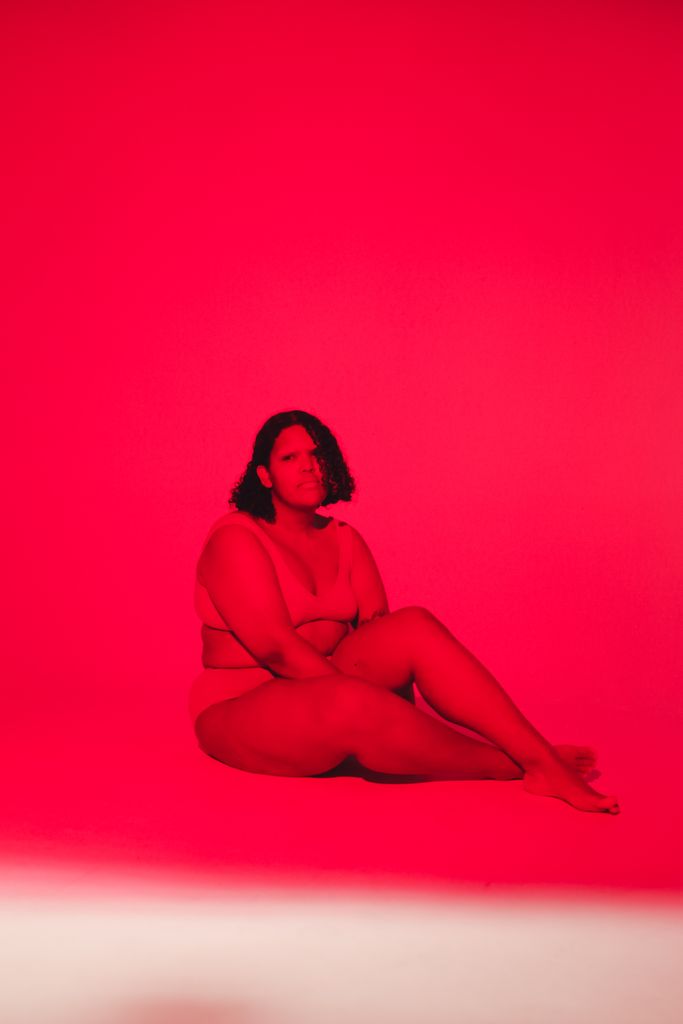 Artistic studio shot of a plus-size woman seated under vibrant red lighting, embodying body positivity.