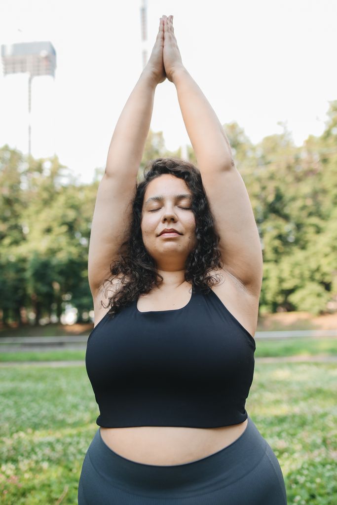 Plus size woman practicing yoga in a serene park setting, enjoying wellness and relaxation.