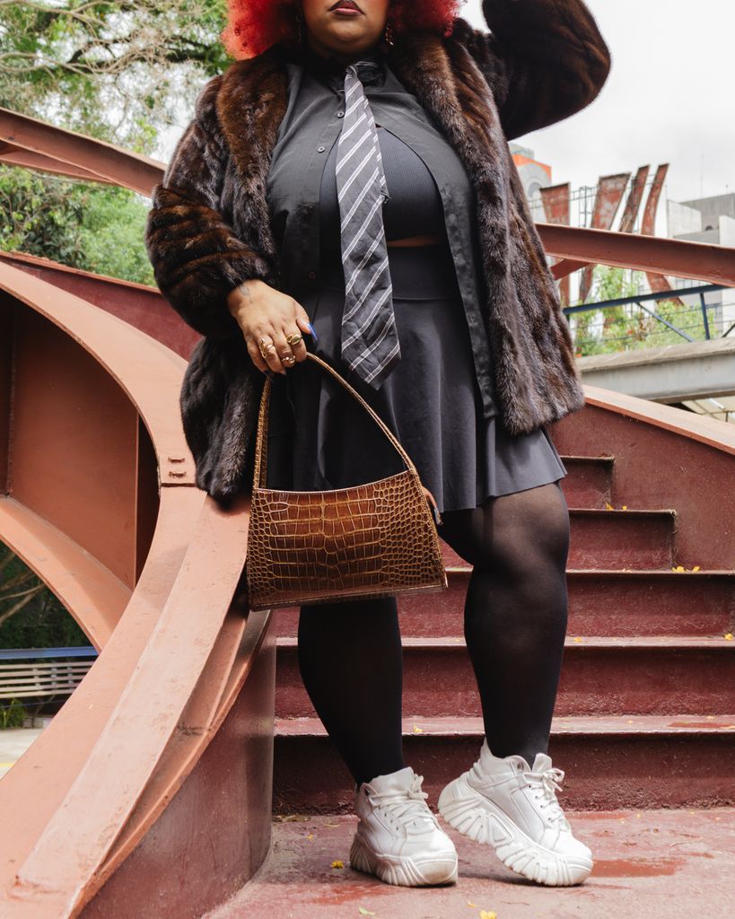 Stylish woman with pink hair, fur coat, and handbag on outdoor staircase in São Paulo.